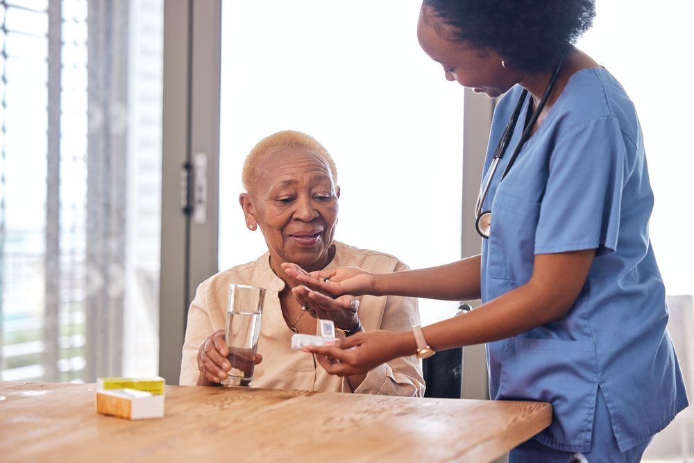 Nurse helping an older woman with her daily medication at the kitchen table