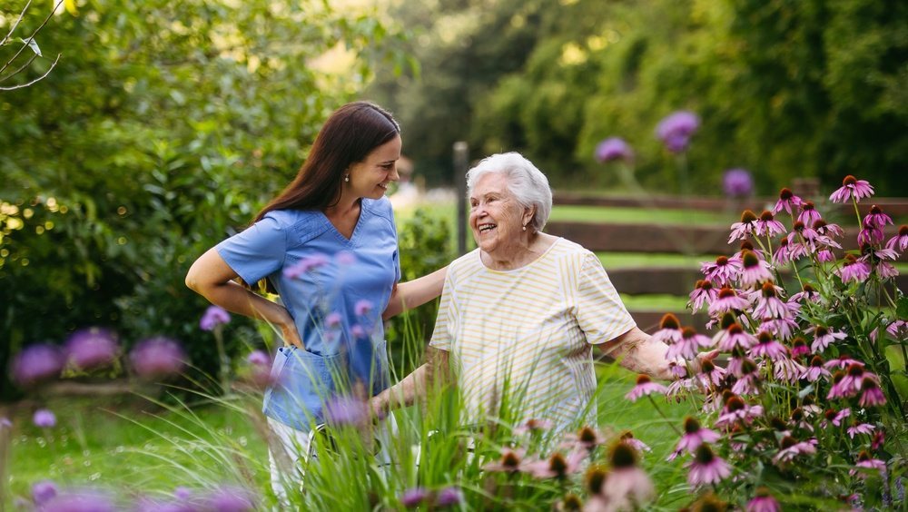 Caregiver and smiling older woman walking together through a flower garden
