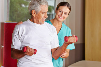 therapist assisting senior man with dumbbells