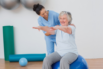 physical therapist assisting a senior woman sitting on an exercise ball