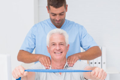 male physiotherapist assisting senior man in exercising with resistance band